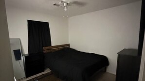 A hotel room with a bed, a desk, a chair, a wardrobe, a ceiling fan, and a window with curtains.