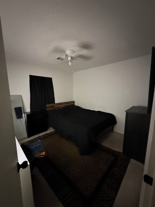 A hotel room with a bed, a desk, a chair, a wardrobe, a ceiling fan, and a window with curtains.