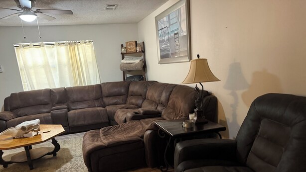 A living room with a sectional sofa, a coffee table, a lamp, and a ceiling fan.