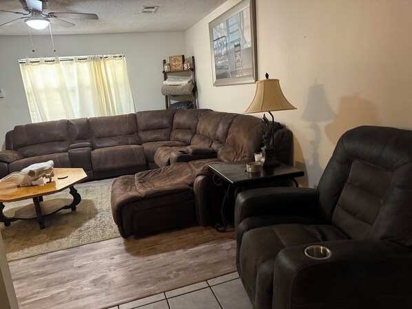 A living room with a sectional sofa, a coffee table, a lamp, and a ceiling fan.