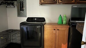 A kitchen with a washing machine, a refrigerator, wooden cabinets, and a tiled floor.