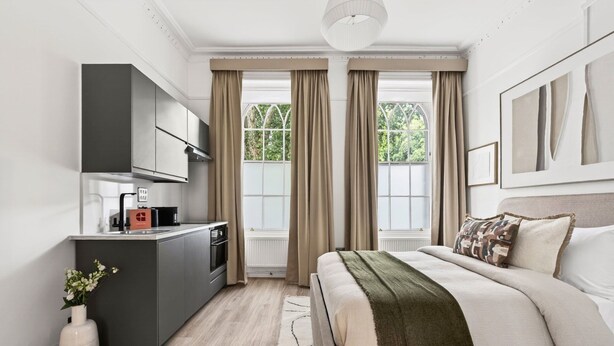 A modern bedroom with a bed, bedside table, and a kitchenette area. - GuestReady - Bright Double Room in Central London (London)