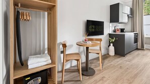 A modern room with a wooden wardrobe, a round wooden table with two chairs, a small kitchen area, and a 'Guest Ready' sign. - GuestReady - Bright Double Room in Central London (London)