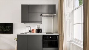 A compact kitchen with dark cabinetry, a built-in oven, and a coffee machine. - GuestReady - Bright Double Room in Central London (London)