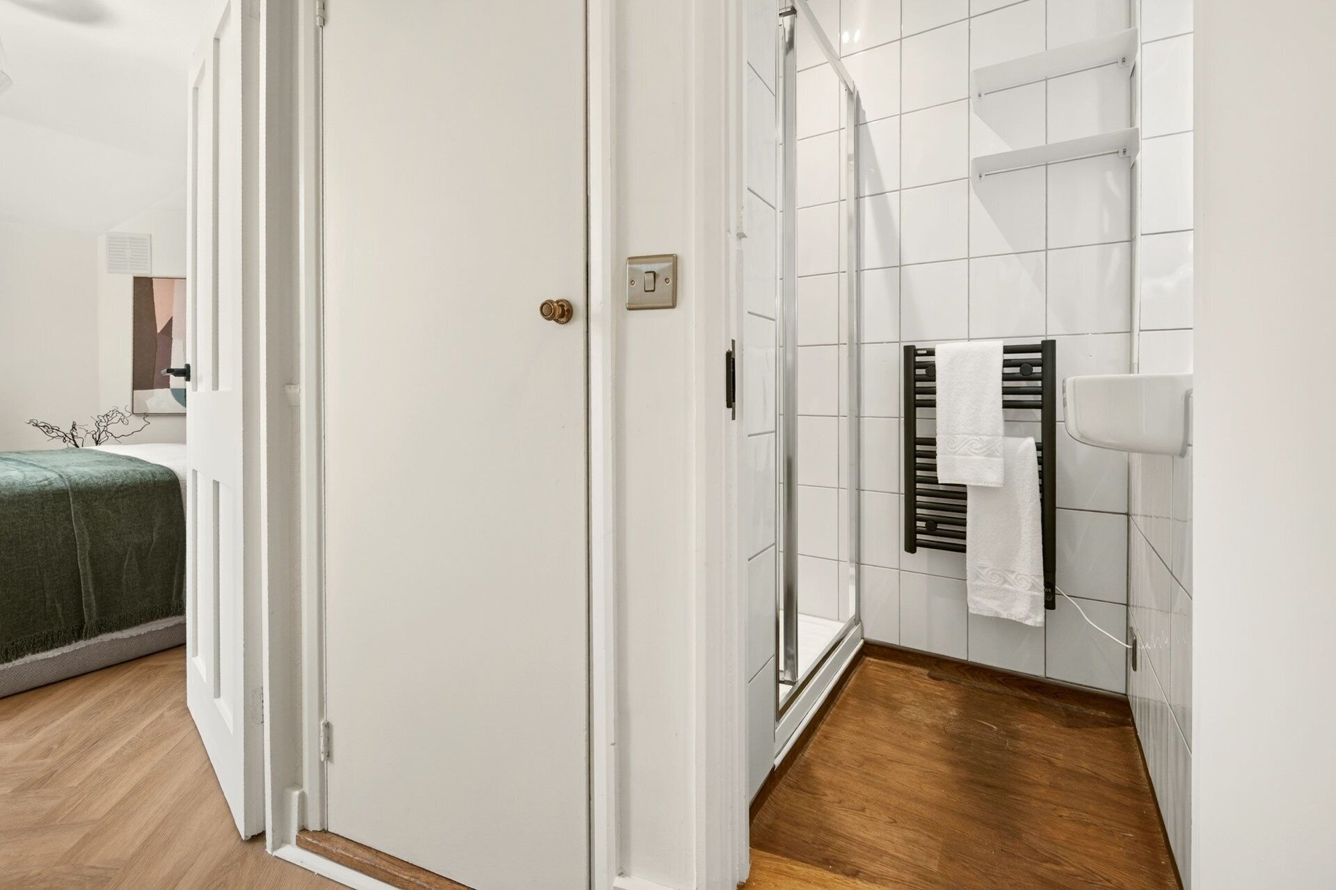 Une salle de bain avec des carreaux blancs, un porte-serviettes, une douche et un plancher en bois.
