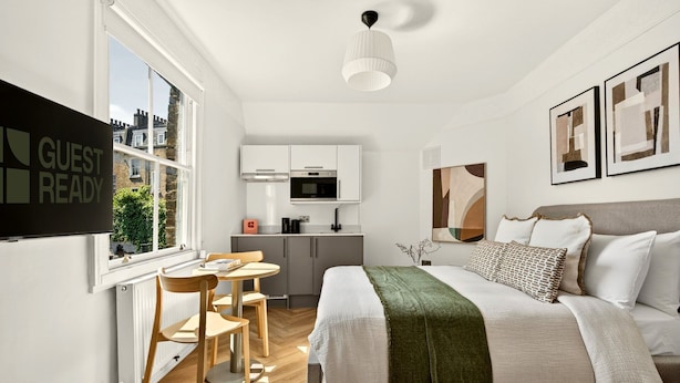 A modern hotel room with a bed, a dining table with chairs, a kitchen area, and artwork on the walls. - GuestReady - Modern Double En-Suite in WC1 (London)