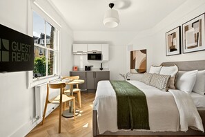 Een moderne hotelkamer met een bed, een eettafel met stoelen, een keukenhoek en kunst aan de muren.