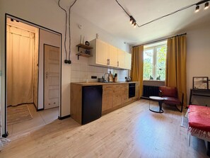 A modern kitchen with wooden cabinets, a built-in dishwasher, and a window with curtains. - Nowowiejska Green Escape Apartment (Wrocław)