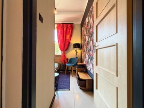 A hallway with a wooden door, a blue chair, a small table, a lamp, and a bed with a purple rug. - Nowowiejska Green Escape Apartment (Wrocław)