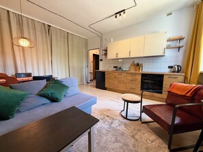 A modern living room with a sofa, a table, a chair, and a kitchen area with cabinets and appliances. - Nowowiejska Green Escape Apartment (Wrocław)