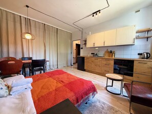 A modern room with a bed, a dining table, chairs, a kitchen area with cabinets and appliances, and a large window with curtains. - Nowowiejska Green Escape Apartment (Wrocław)
