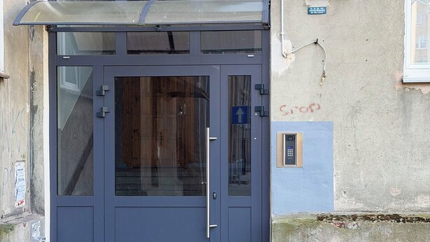 Eine dunkelblaue Tür mit Glasfenster, einer Metallhandle und einem kleinen Schild mit der Adresse '70'.