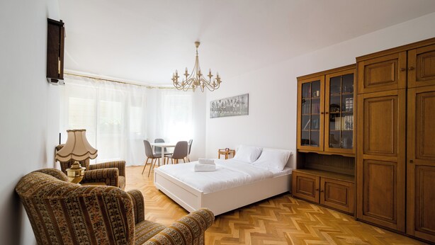 Une chambre à coucher comprenant un lit, une armoire en bois, un lustre, un bureau avec des chaises et des fauteuils à motifs.