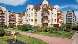Un immeuble résidentiel à plusieurs étages, doté de balcons, d’une allée pavée et d’une aire de jeux.