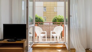 Un balcon équipé d’un téléviseur, de deux chaises et offrant une vue sur un immeuble et des espaces verts.