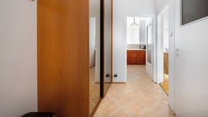Un couloir avec une porte en bois, un porte-manteau et, au fond, un coin cuisine.