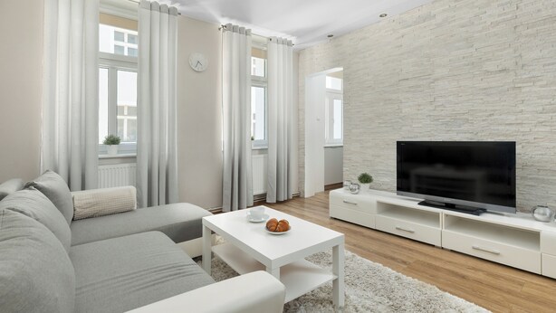 Een moderne woonkamer met een bank, salontafel, televisie en een wand met een stenen textuur.