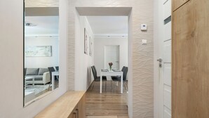 Een hal met een houten bankje, een eetruimte met een tafel en stoelen, en een witte deur.