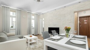 Een moderne woonkamer met een witte bank, een eettafel voor twee personen, een flatscreen televisie en een open haard.