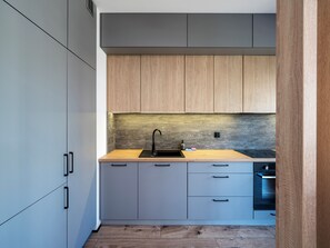 A modern kitchen with grey cabinets, a wooden countertop, and a built-in oven. - Kopcińskiego Deluxe Studio (Łódź)