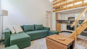 Een moderne woonkamer met een groene bank, een houten salontafel en een keuken met witte kasten en een fornuis.