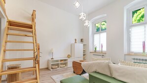 Een kamer met een houten ladder, witte planken, een groene bank en een open haard.