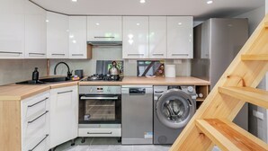 Een kleine keuken met witte kastjes, een inbouwoven, een wasmachine en een houten aanrecht.