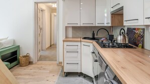 Een kleine keuken met witte kastjes, een houten aanrecht, een waterkoker en een fornuis.