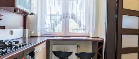 A kitchen with a stove, a window with curtains, and two stools.