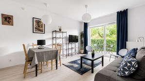 Ein modernes Wohnzimmer mit Essbereich, einer Couch, einem Fernseher und einem großen Fenster mit Vorhängen.