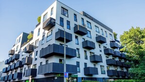 Ein modernes, mehrstöckiges Gebäude mit Balkonen, bewölkter Himmel und einem Wegweiser.