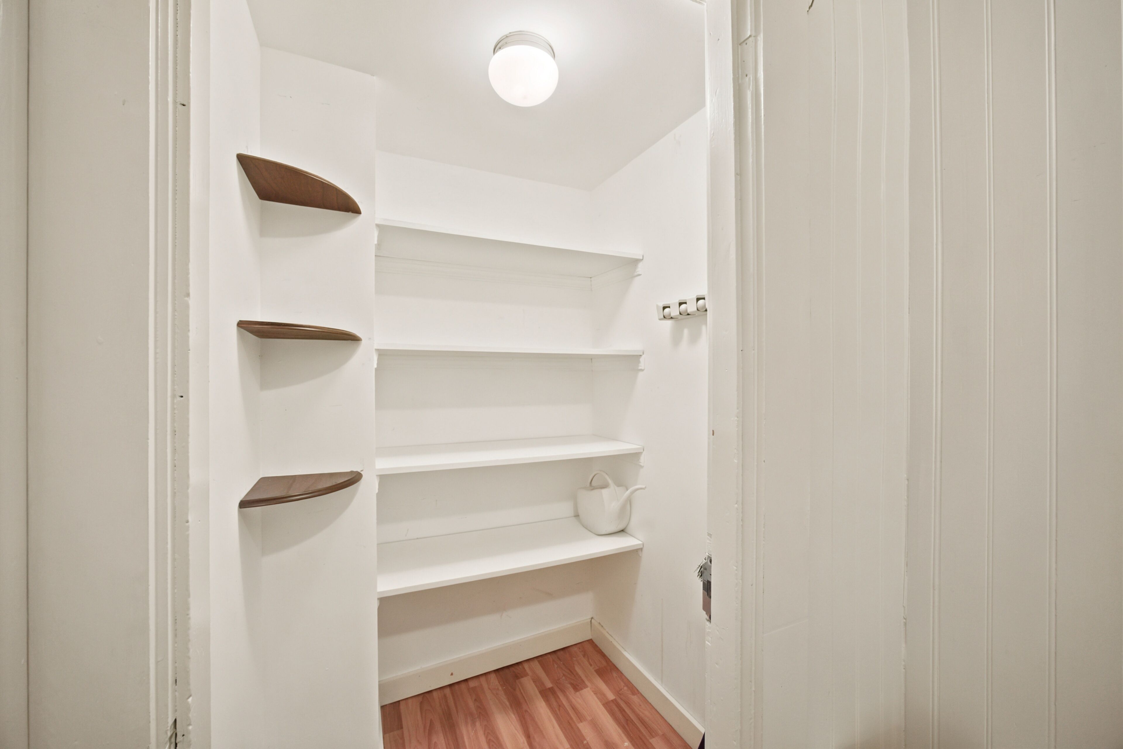 A narrow hallway with white walls, wooden shelves, and a white door.