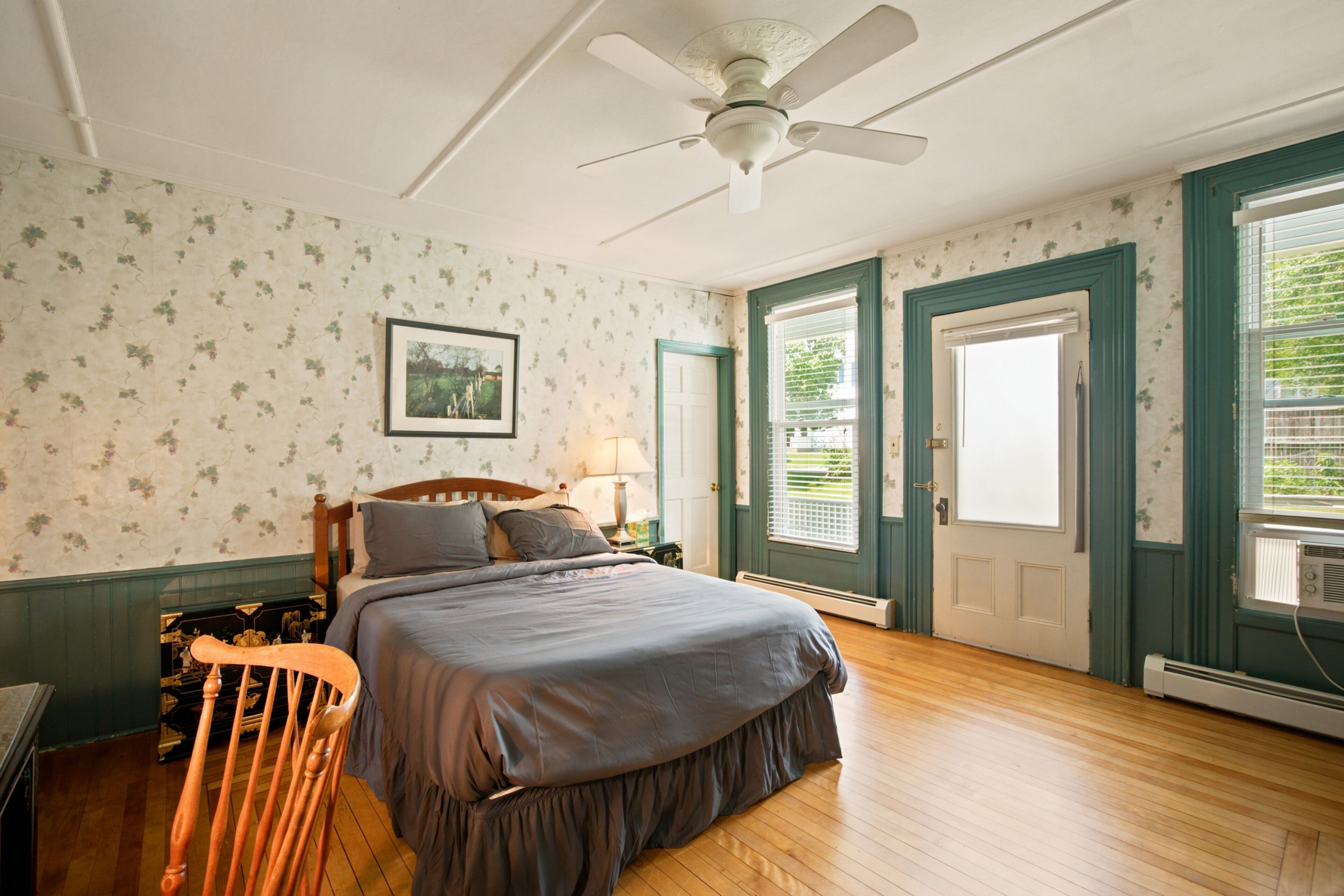A bedroom with a bed, a ceiling fan, a dresser, and a window with shutters.