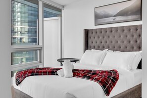 Een hotelkamer met een bed, een raam met uitzicht op gebouwen, een hoofdbord en een schilderij aan de muur.