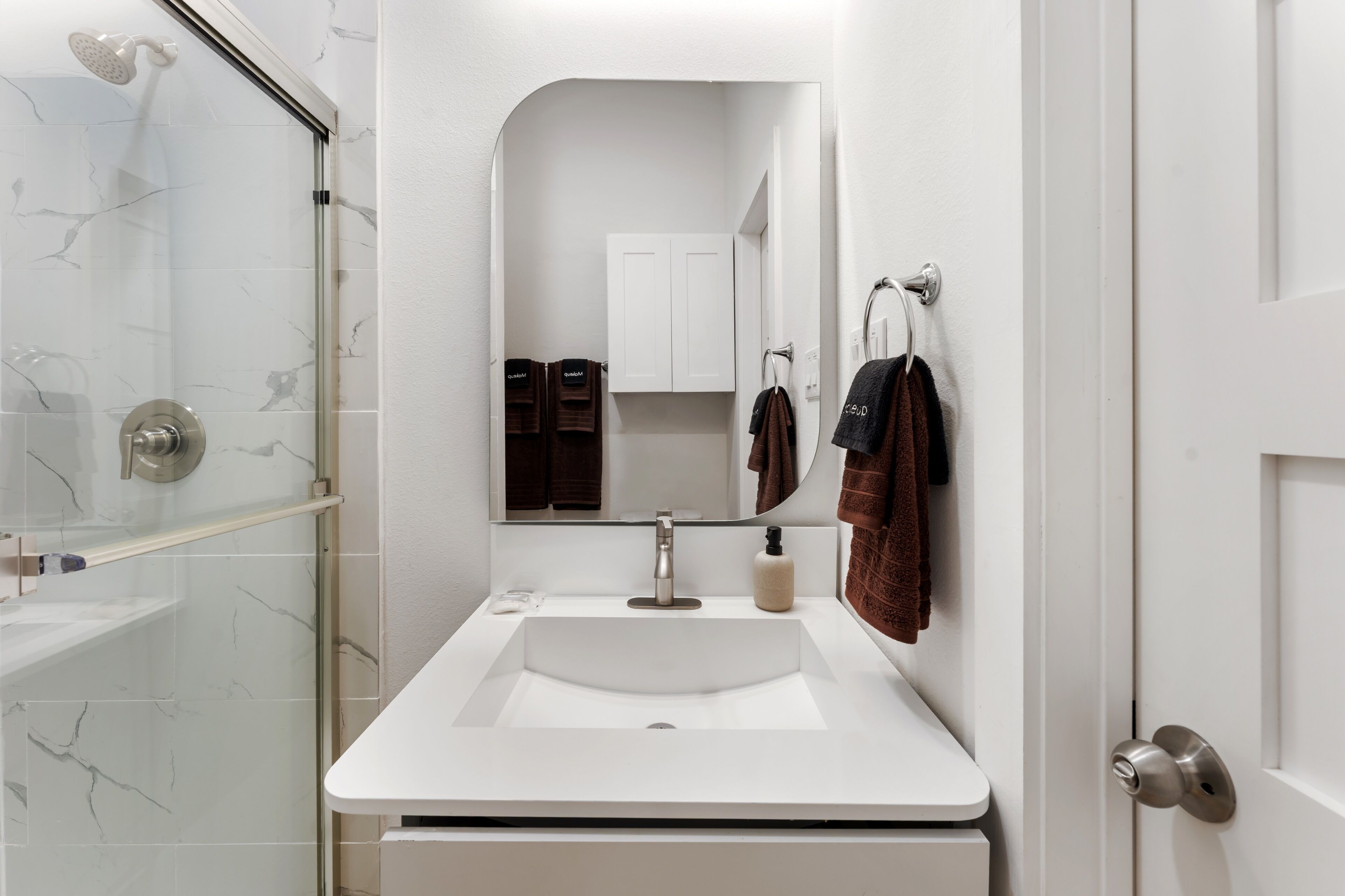 A bathroom with a glass shower enclosure, a white sink, a mirror, and a towel rack.