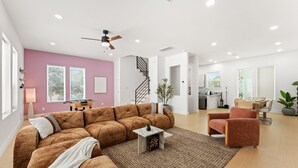 Ein modernes Wohnzimmer mit einem Ecksofa, einem kleinen Beistelltisch, einer Treppe und einer Küchenzeile.