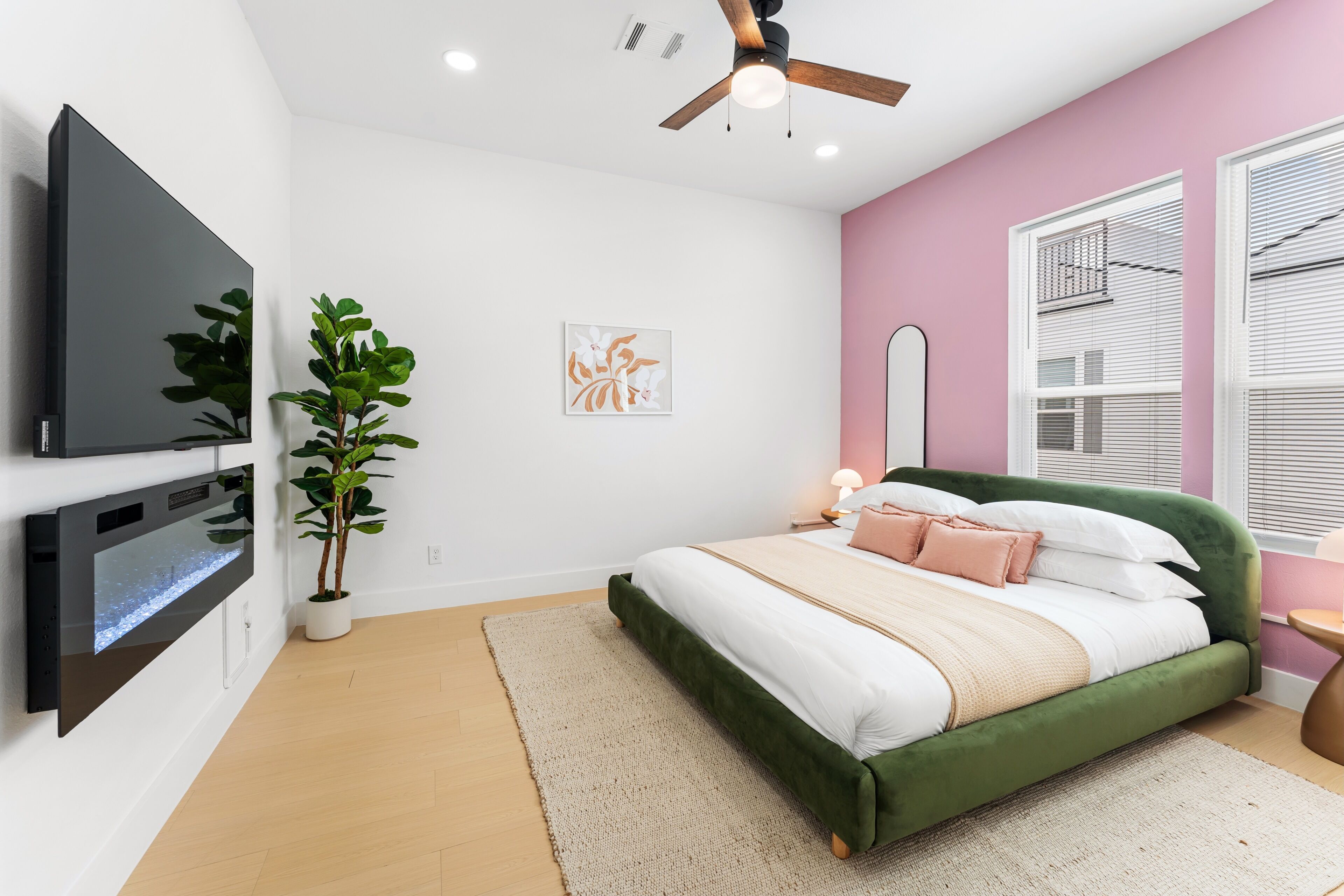 Ein modernes Schlafzimmer mit einem grünen Bett, einem flachbildfernseher an der Wand, einer Zimmerpflanze und einem Deckenventilator.