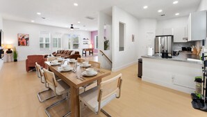 Eine moderne Küche mit Edelstahlgeräten, ein Essbereich mit Holztisch und Stühlen sowie ein Wohnzimmer mit Sofa und Couchtisch.