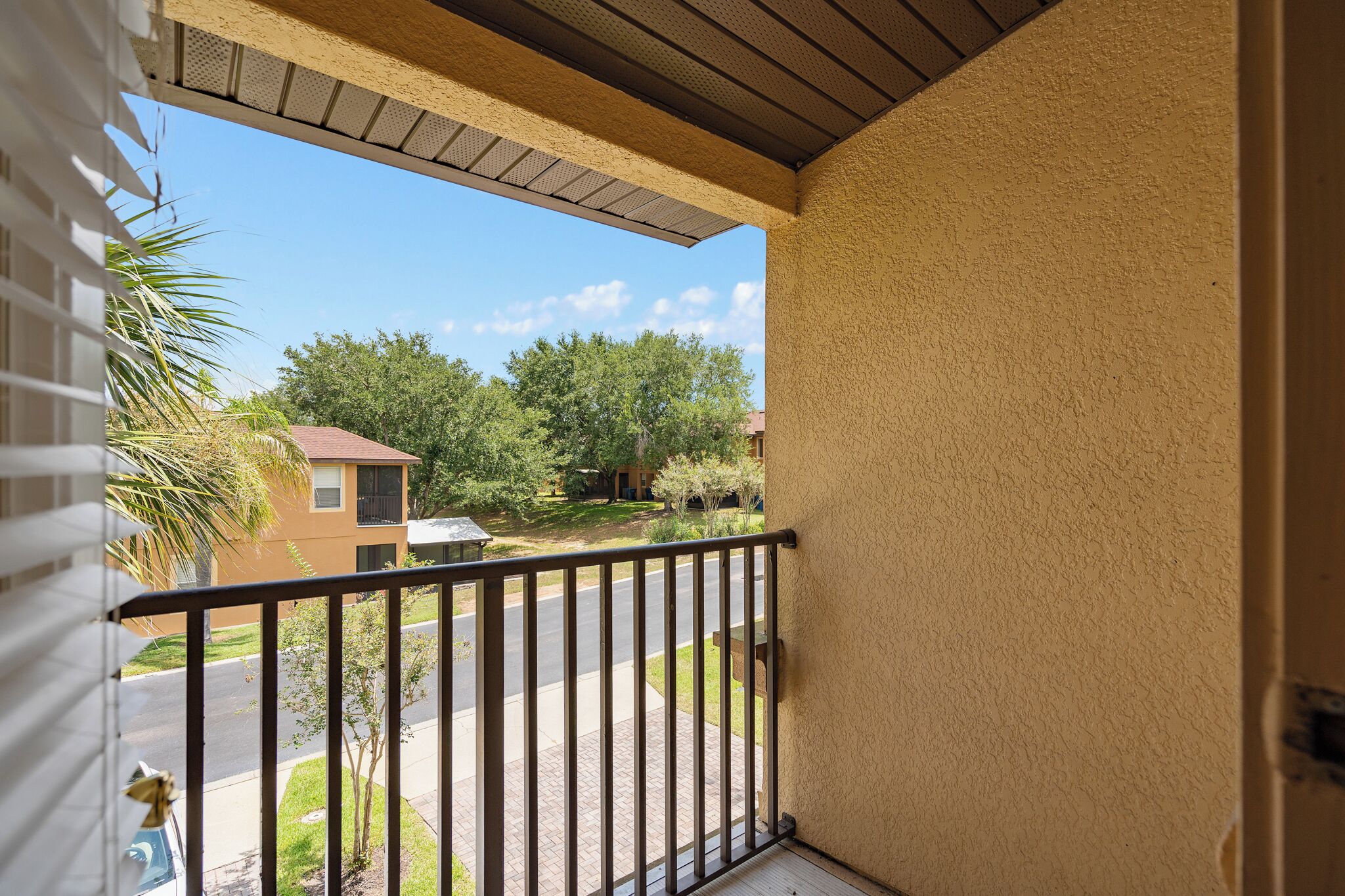 A balcony with a view of a residential street, a house, and a palm tree.