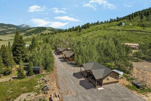 A row of cabins in a mountainous area with a dirt road leading to them.