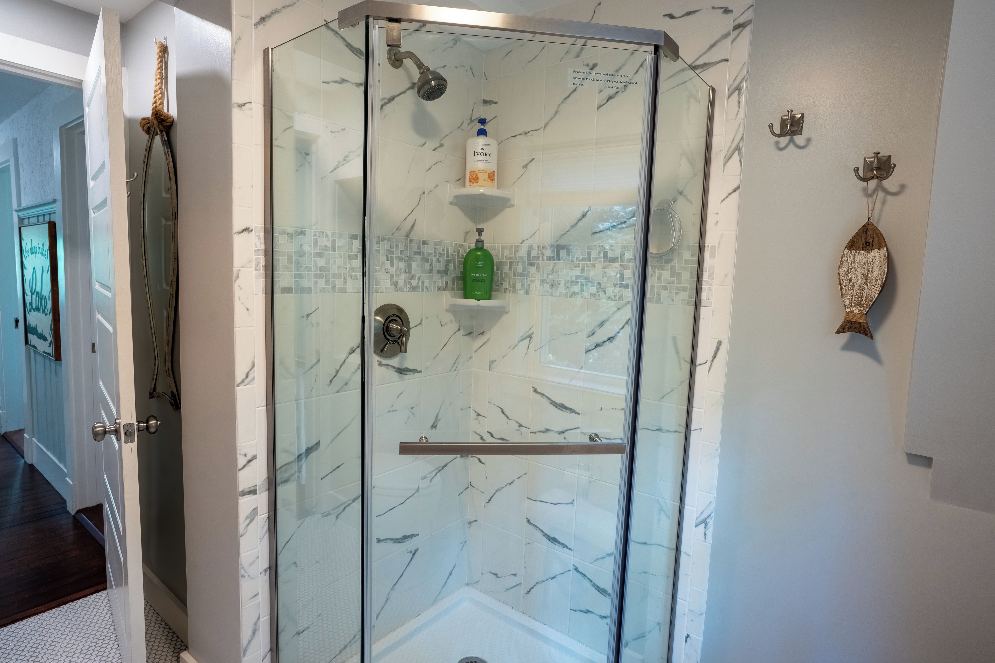 A glass-enclosed shower with a marble backsplash, a hand soap dispenser, and a towel rack.
