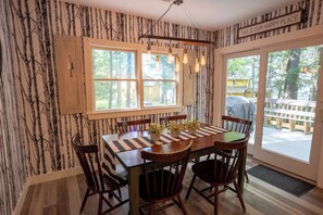 A dining area with a wooden table, six chairs, and a view of the outdoors through large windows.