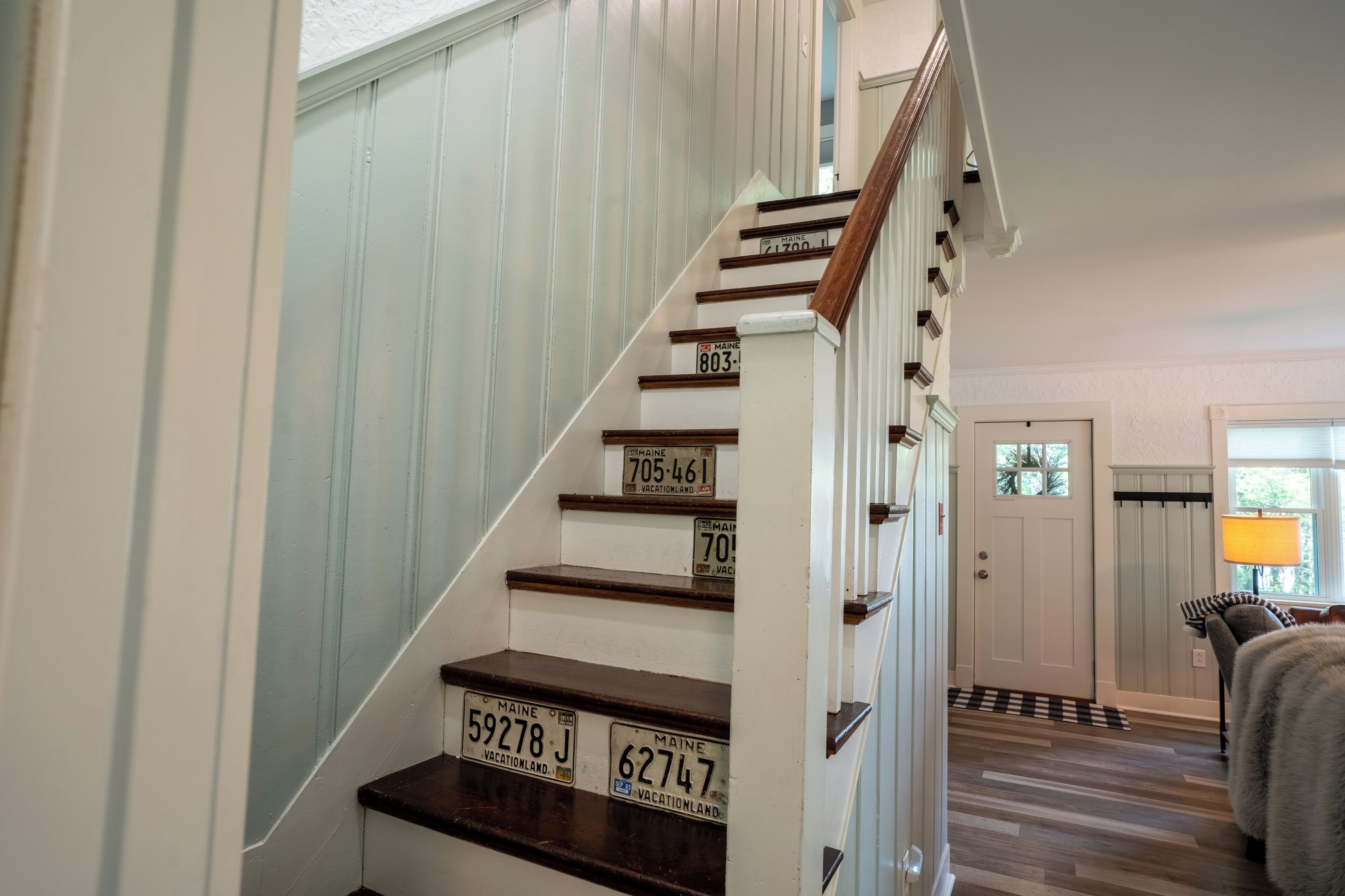 Una escalera de madera con paredes blancas que lleva a una habitación con una puerta y un ventanal.