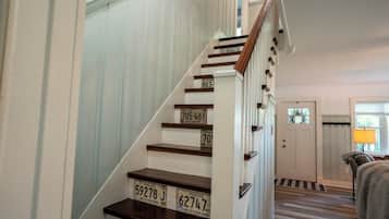 Una escalera de madera con paredes blancas que lleva a una habitación con una puerta y un ventanal.