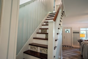 Una escalera de madera con paredes blancas que lleva a una habitación con una puerta y un ventanal.