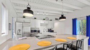 Una cucina moderna con mobili bianchi, elettrodomestici in acciaio inossidabile e un'isola centrale con sedie.