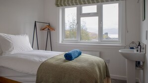 A bedroom with a bed, a window with a view, a bedside table, and a bathroom with a sink.