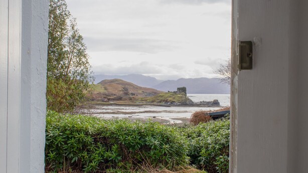 A coastal landscape with a grassy hill, a body of water, and a stone structure.