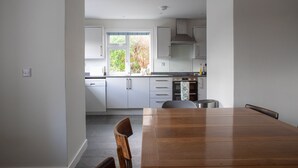 A modern kitchen with white cabinets, a wooden dining table, and a window with a view of greenery.