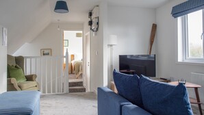 A modern living room with a sofa, a chair, a television, and a staircase leading to a bedroom.
